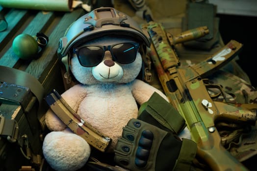 teddy bear in a military helmet among a pile of military ammunition, a rifle, grenades, a bulletproof vest, a helmet and other tactical airsoft items