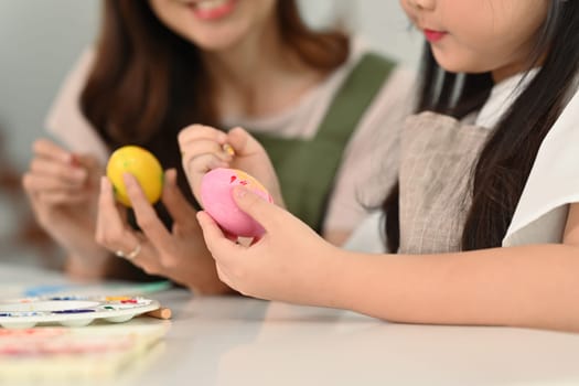 Cropped shot mother and her daughter painting easter eggs in living room. Happy easter concept.