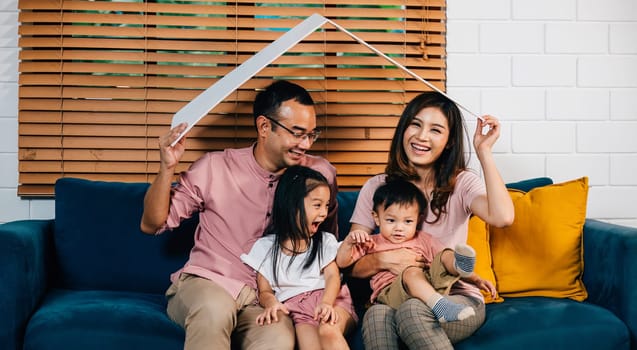 In their new house a smiling family sits on the sofa holding a cardboard roof mockup representing security and happiness during their home relocation. The key is family support and planning.