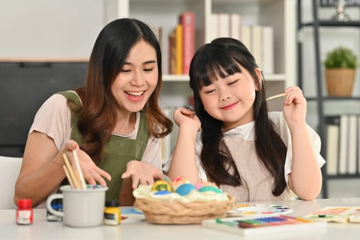 Cute little child girl and mother coloring easter eggs in living room. Preparation for holiday concept.