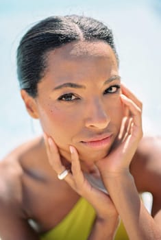 Young woman in a swimsuit sits in the sun resting her chin on her hands. High quality photo