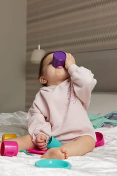 happy cute little child girl playing and pretending drinking tea from toy cups on bed