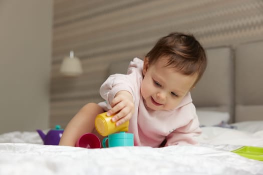 happy cute little child girl playing and pretending drinking tea from toy cups on bed