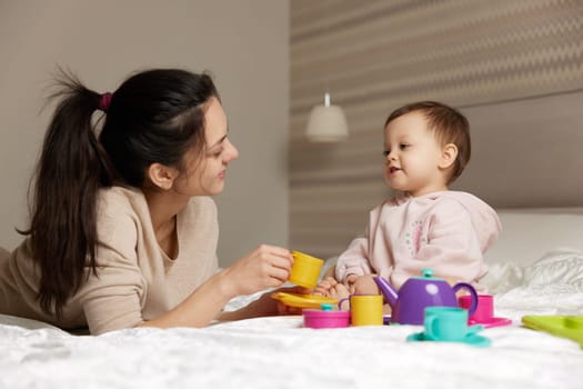 beautiful mother and little child daughter playing tea party in bedroom