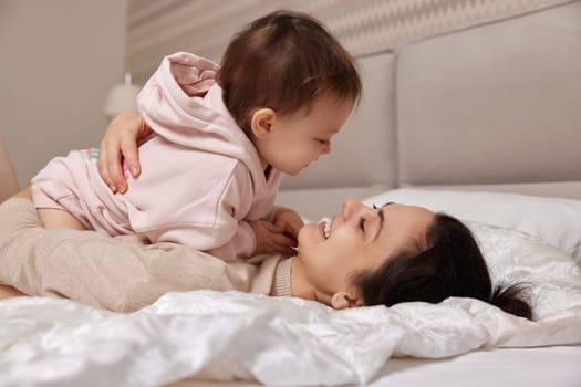 happy mother playing with her cute baby daughter on bed in bedroom. loving family having fun