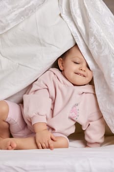 cute funny baby girl hiding under blanket on the bed