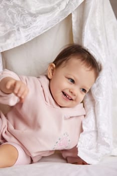 cute funny little child girl looks out from under the blanket on the bed