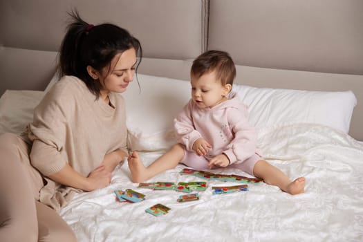 pretty mother playing with puzzle pieces with her little child girl in bedroom