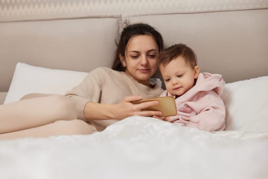 Caucasian mother and child playing online game on smartphone in bedroom at home