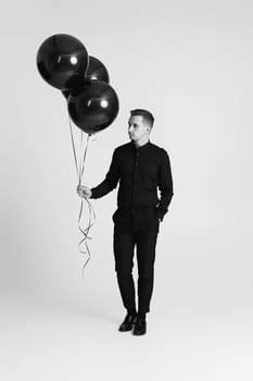 elegant caucasian man with bunch of black air balloons on white background. black and white