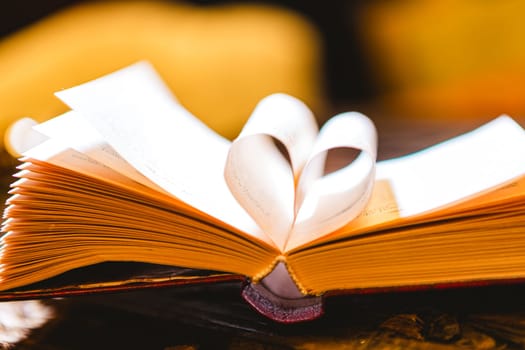 Stack of books in the colored cover lay on the table. Open book with curled leaves in the shape of a heart. Library, education. Love of books, reading. Empty space for Your text on the left. Shallow dof