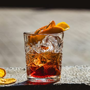 Delicious old fashion cocktail in the etched glass with ice and orange slices, dark wooden background. Shallow dof