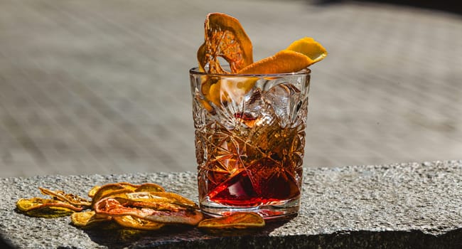 Delicious old fashion cocktail in the etched glass with ice and orange slices, dark wooden background. Shallow dof