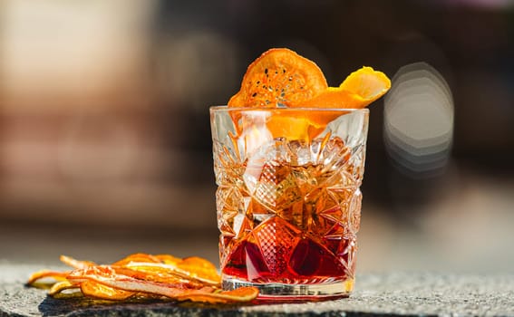 Delicious old fashion cocktail in the etched glass with ice and orange slices, dark wooden background. Shallow dof