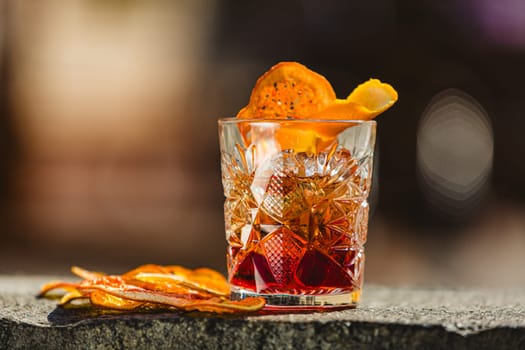 Delicious old fashion cocktail in the etched glass with ice and orange slices, dark wooden background. Shallow dof