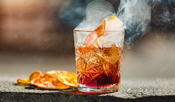 Delicious old fashion cocktail in the etched glass with ice and orange slices, dark wooden background. Shallow dof