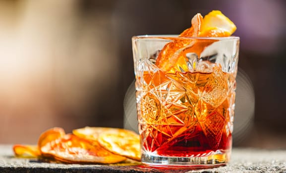 Delicious old fashion cocktail in the etched glass with ice and orange slices, dark wooden background. Shallow dof