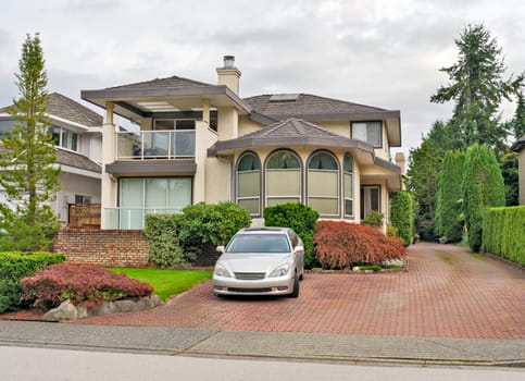 Big residential house with a car parked on pawed drvieway in front.