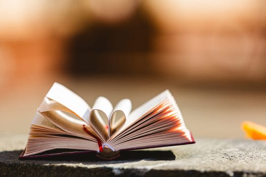 Stack of books in the colored cover lay on the table. Open book with curled leaves in the shape of a heart. Library, education. Love of books, reading. Empty space for Your text on the left. Shallow dof