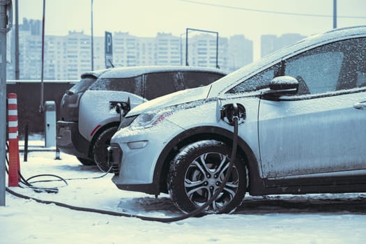 Charging electric car on the street. Electric car in snow on charging spot, cold conditions