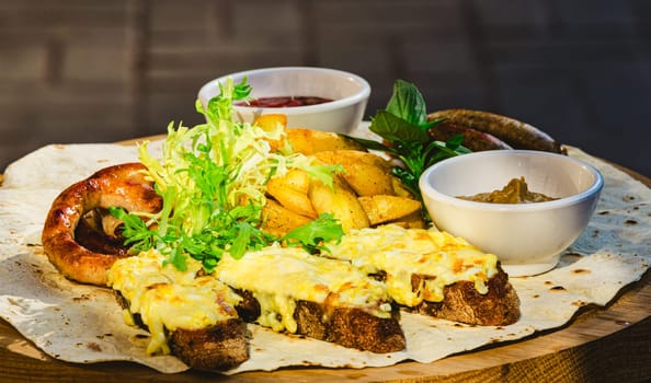 German style grilled sausages with potato wedges and bread with cheese and sauces close-up on a wooden tray on the table. Shallow dof