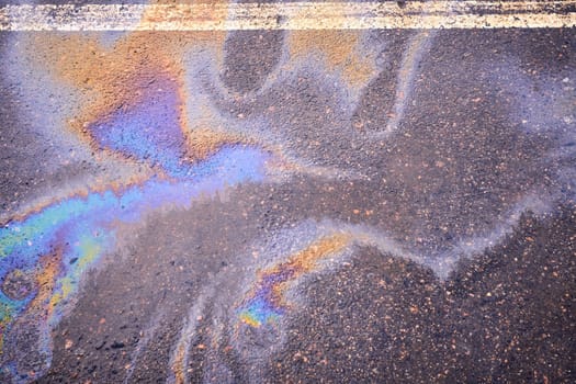 Fuel or oil spills on an asphalt road after melted snow as a texture or background