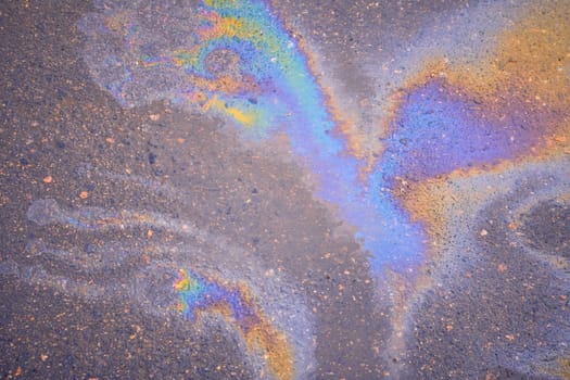 Texture of colorful petrol oil spill on wet pavement. Slick industry oil fuel spilling water pollution.