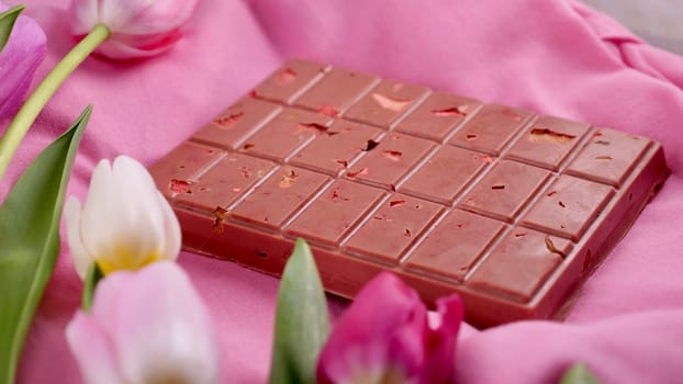 A bar of pink ruby chocolate with sublimated freeze-dried strawberries and almonds and spring tulip flowers . A dessert based on berries and nuts for International Women's Day, March 8, mother's day