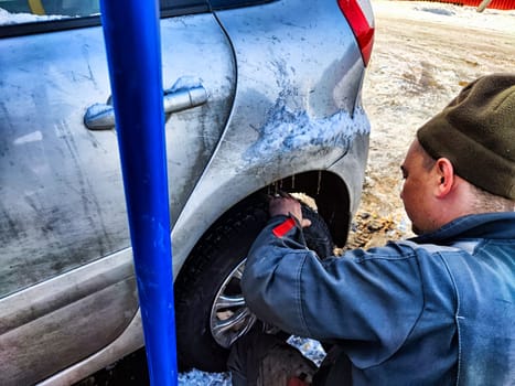 Ishim, Russia - November 27, 2023: man makes tire of car wheel before cold snow season. Experienced mechanic changes wheel of car. The driver prepares a classic car for driving in the snow in winter