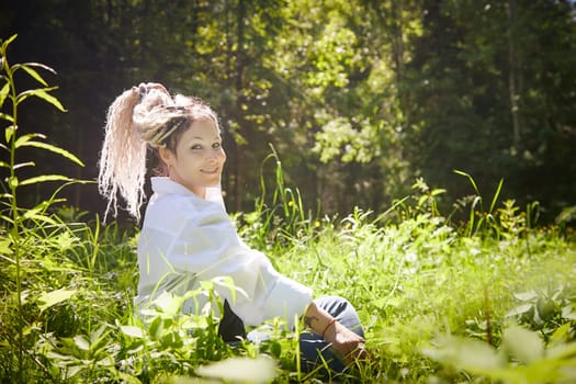 Kirov, Russia - June 12, 2023: Hippy girl enjoys life in forest on a sunny spring or summer day. Woman in green nature landscape