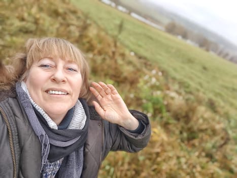 Happy female blonde tourist taking selfie picture with smart mobile phone outside. Middle aged woman having fun on adventure nature trip