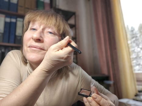 Portrait of a middle-aged woman doing eye makeup. Selfie portrait of lady who is businesswoman, accountant, manager, freelancer doing morning makeup at office on working place