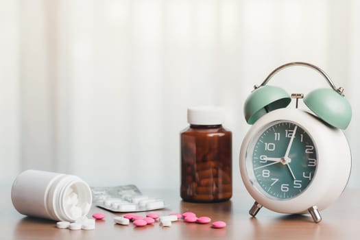 Healthcare essentials with an alarm clock, pills, and medicine bottle on a white curtain background for time management, deadlines, and the concept of medical and health care 