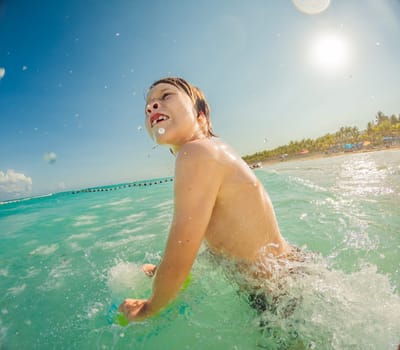 Joyful boy plays in the sea, creating playful splashes and enjoying the waves.