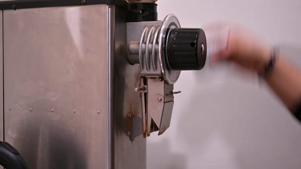 Hand of a barista extracting coffee from a coffee grinder.