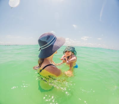 Mother and newborn son share a serene swim in the sea, creating timeless memories by the water's embrace.