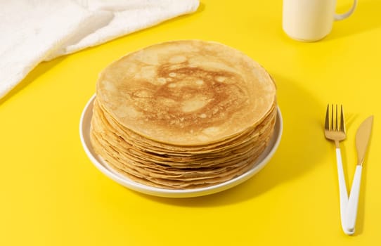 A stack of thin pancakes on a yellow table.