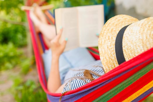Woman enjoying a book in a hammock on a sunny day, with straw hat and garden background.