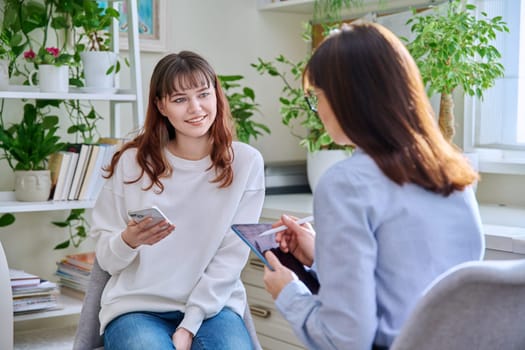 Teenage girl college student at therapy meeting with mental health professional social worker psychologist counselor sitting together in office. Psychology, psychotherapy, mental assistance support