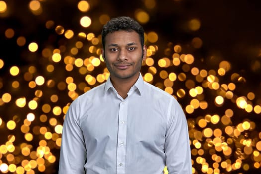 Handsome dark-skinned businessman wearing white shirt looking at camera. Black and golden bokeh lights in the background.