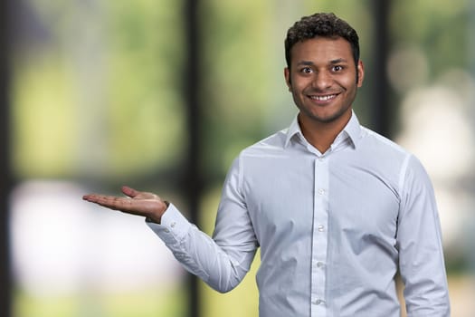 Successful young businessman showing empty space on blurred background. Man showing copy space on blur bokeh background.
