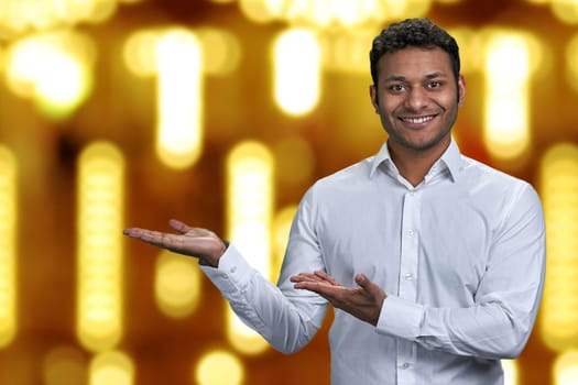 Handsome businessman looking at camera while presenting something on golden bokeh background. Winter holiday special offer.