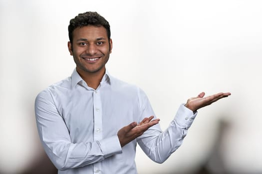 Young handsome man pointing to the side with hand and open palm presenting something. Place for advertisement.