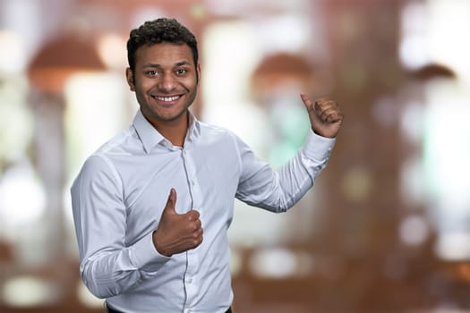 Cheerful guy pointing on copy space behind his back. Indian man pointing with thumb at copy space. Place for your advertisement.