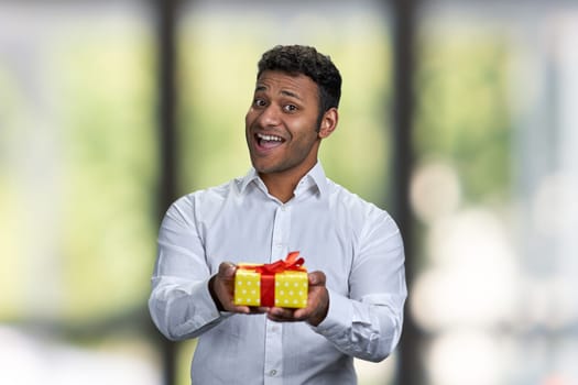 Happy smiling Indian man handing gift box. Abstract blurred background.