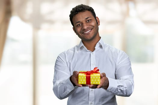 Handsome guy giving gift box on blur interior background. Special holiday offer.