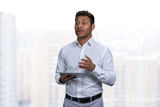 Speaking young manager using computer tablet while giving a presentation. Young indian businessman speaker holding computer tablet.