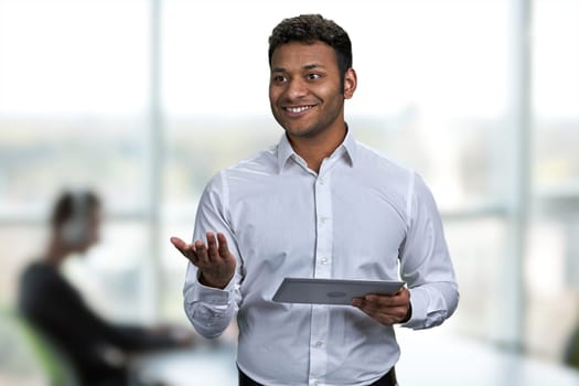 Cheerful businessman wearing white shirt holding digital tablet pc. Blur office interior background.