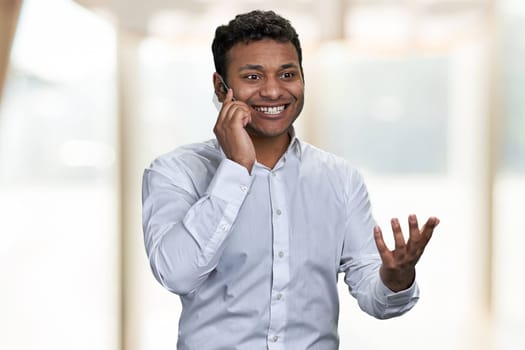 Excited young businessman talking on glass phone on blur interior background. Happy news concept.