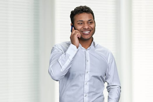 Portrait of happy smiling young businessman talking on mobile phone. Cheerful male executive talks on cell phone indoor.